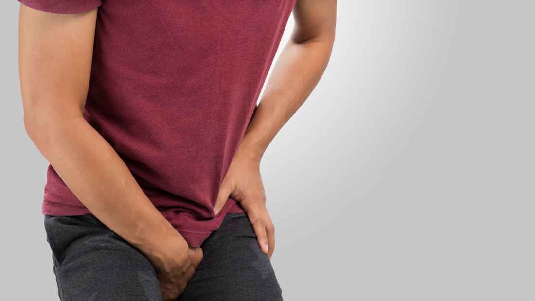 Man in red shirt experiencing discomfort, holding his groin area, illustrating sex toy related injuries.