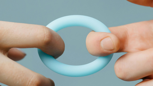 Close-up of hands holding a light blue silicone cock ring, designed for beginners.