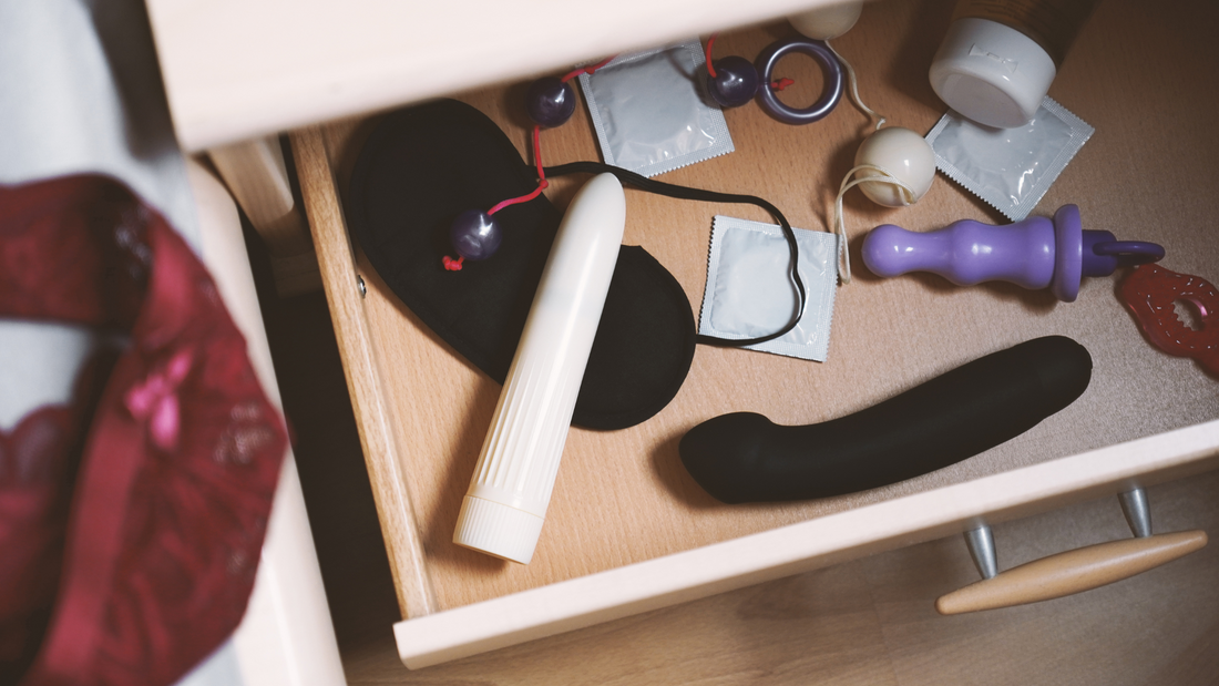 Open drawer containing various sex toys, including vibrators, condoms, an eye mask, and other adult accessories arranged neatly.