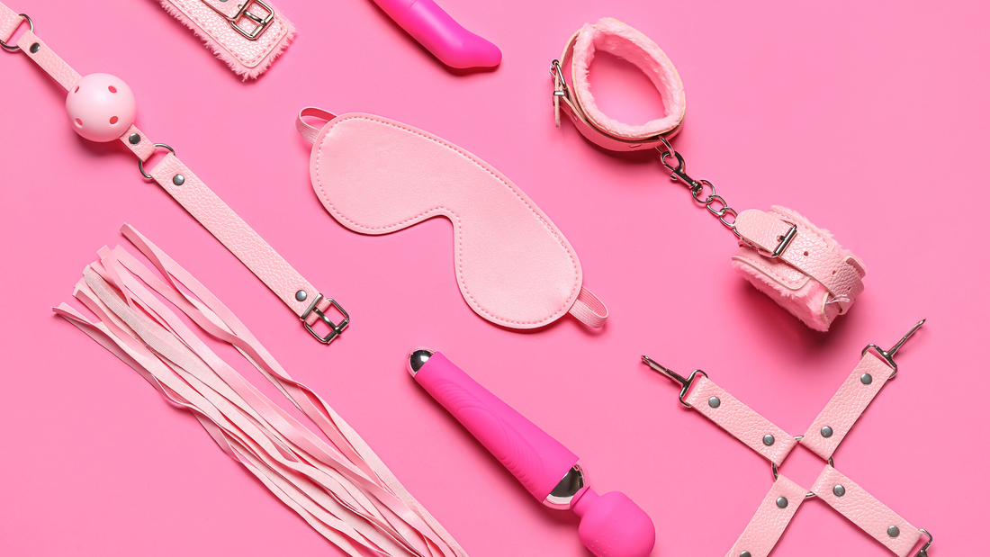 A flat lay of pink BDSM accessories on a pink background, including a blindfold, ball gag, handcuffs, flogger, vibrator, and harness, all designed for adult intimacy and sensual exploration.