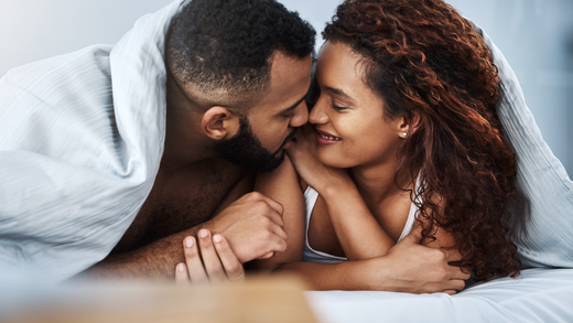Intimate moment between a couple in bed, sharing a close embrace under a white sheet, showcasing a deep emotional connection.