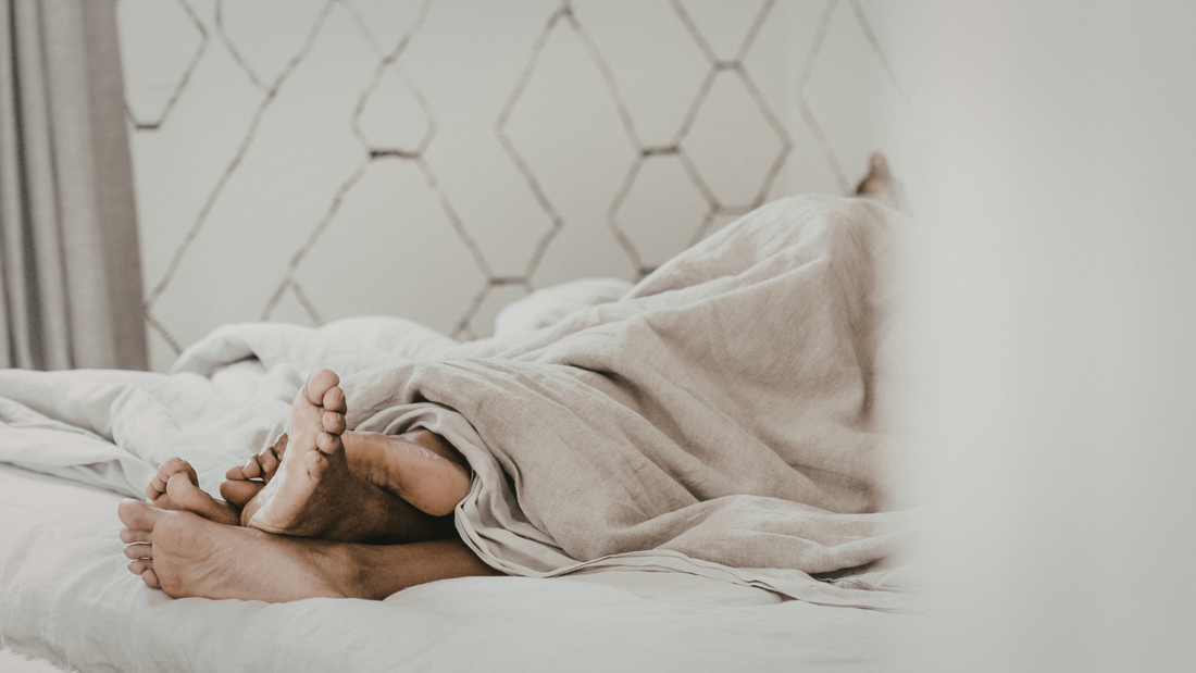 Couple lying together under a duvet in bed, representing intimacy in a long-term relationship