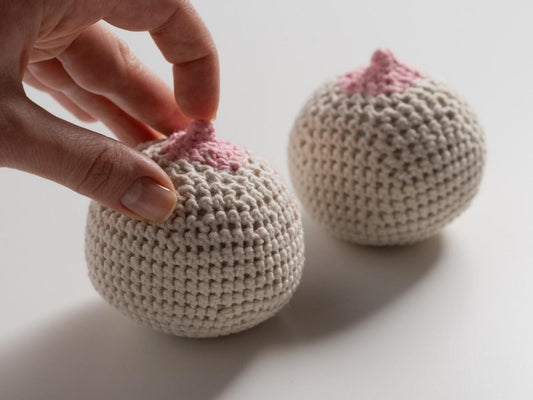 Close-up of two knitted-style nipples with a finger gently touching one, symbolising nipple play and sensitivity.