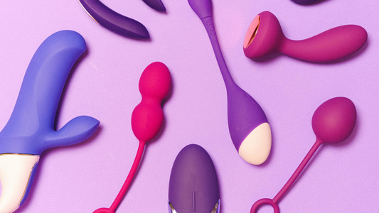 Assorted modern sex toys in purple and pink silicone, including vibrators, Kegel balls and tapping toys, displayed on a soft purple background.