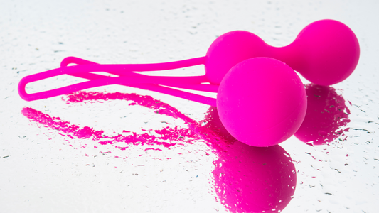 Close-up of bright pink Ben Wa balls made of medical-grade silicone, resting on a wet reflective surface, symbolising intimate wellness and pelvic health.